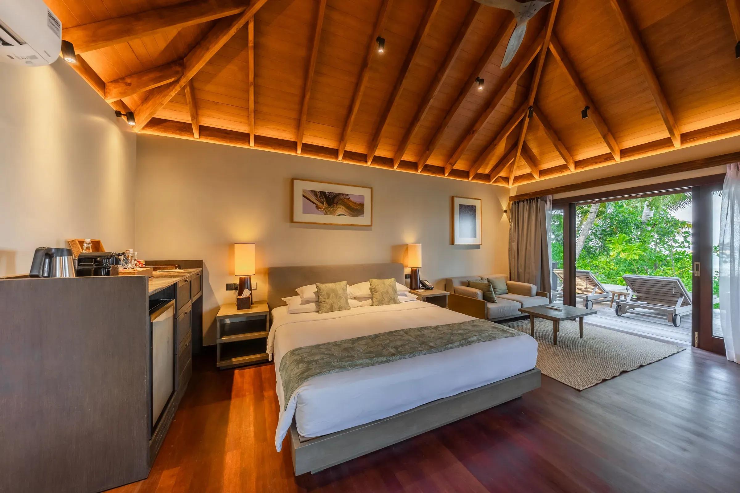 Interno della Beach Villa con letto matrimoniale e terrazza con lettini del Veligandu Island Resort & Spa.
