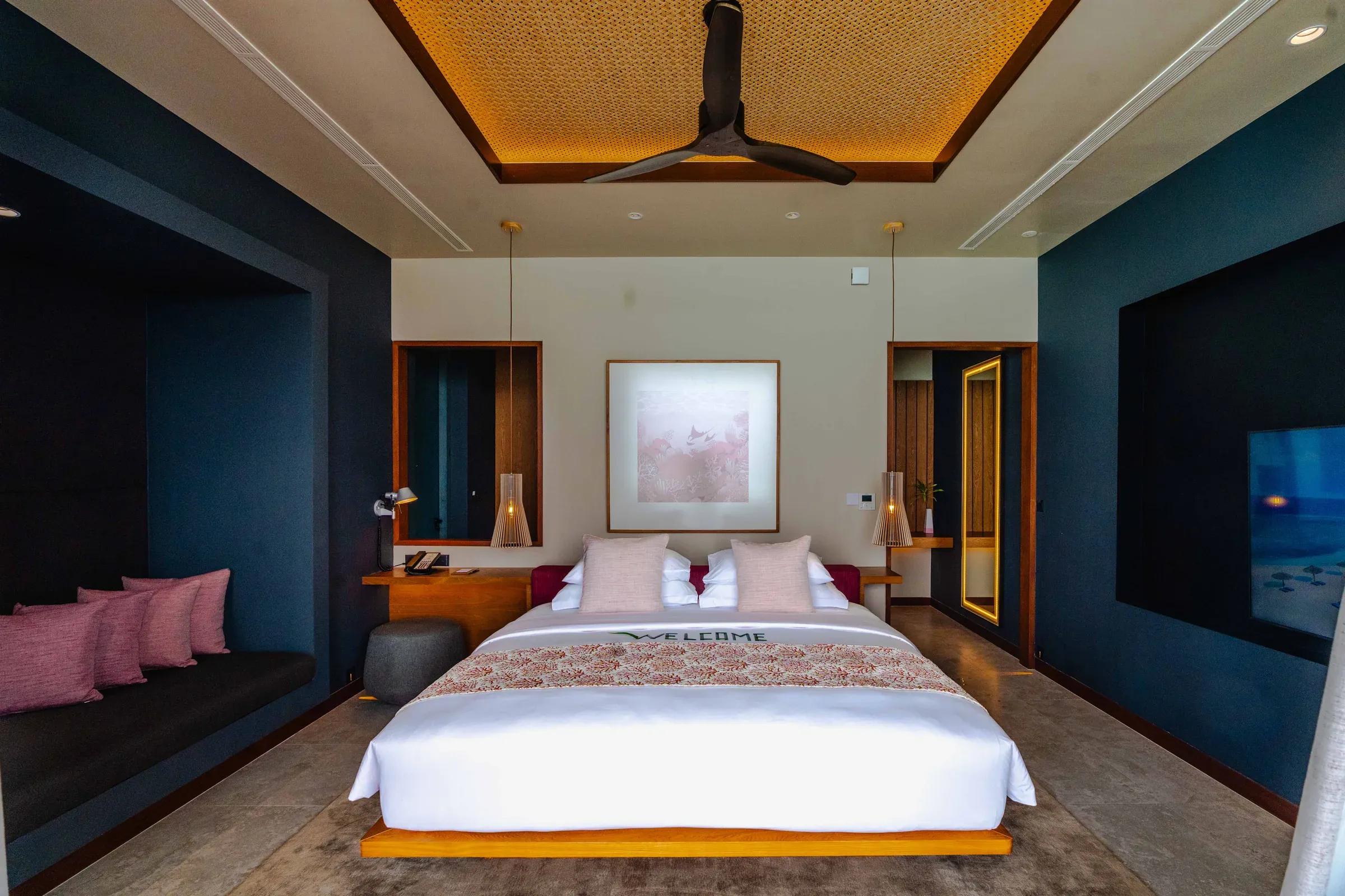 Interno della Ocean Pool Villa con letto matrimoniale e seduta con cuscini del Veligandu Island Resort & Spa.