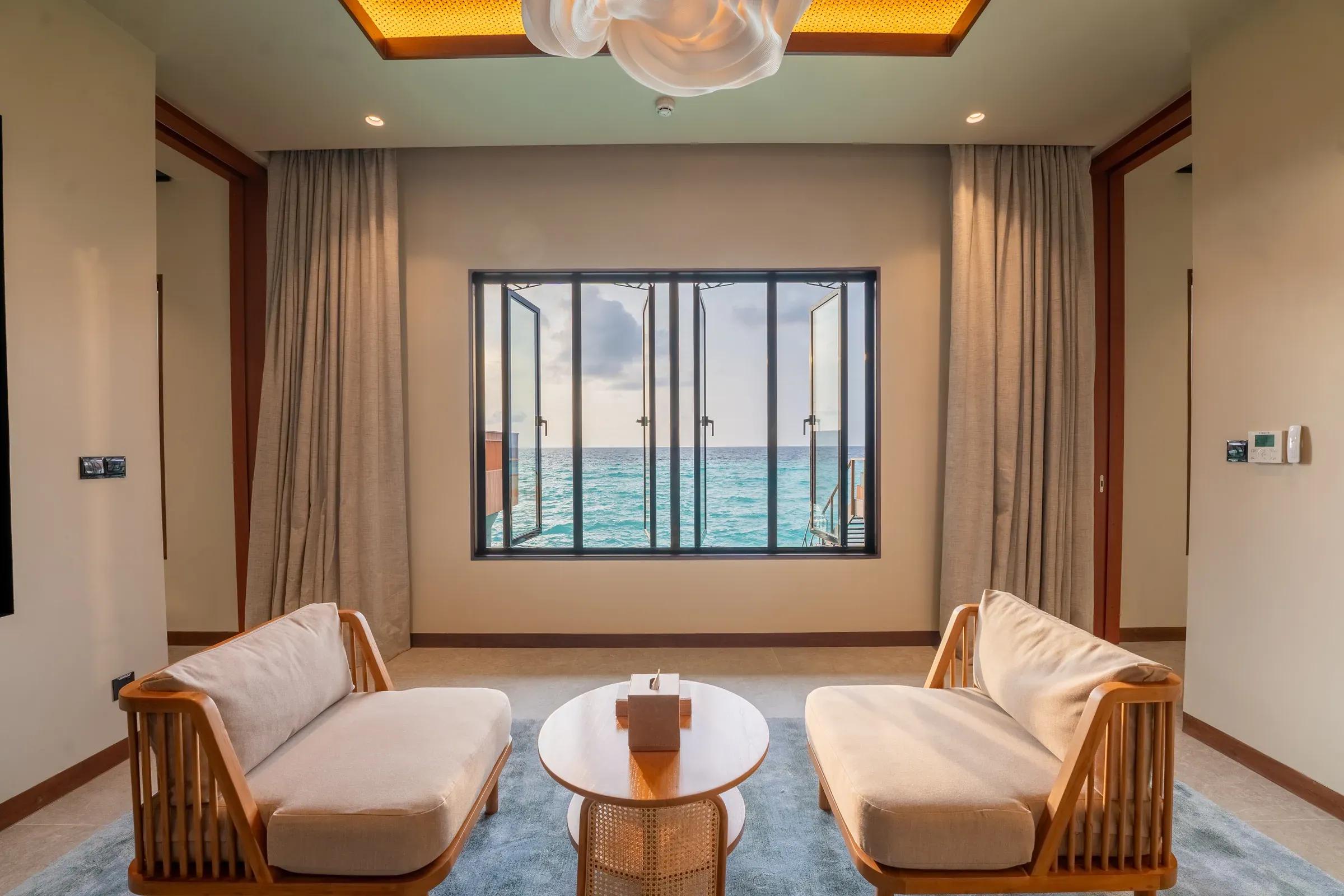 Area soggiorno con divani e finestra con vista mare nella Sunset Ocean Pool Villa 2 Bedroom al Veligandu Island Resort & Spa.