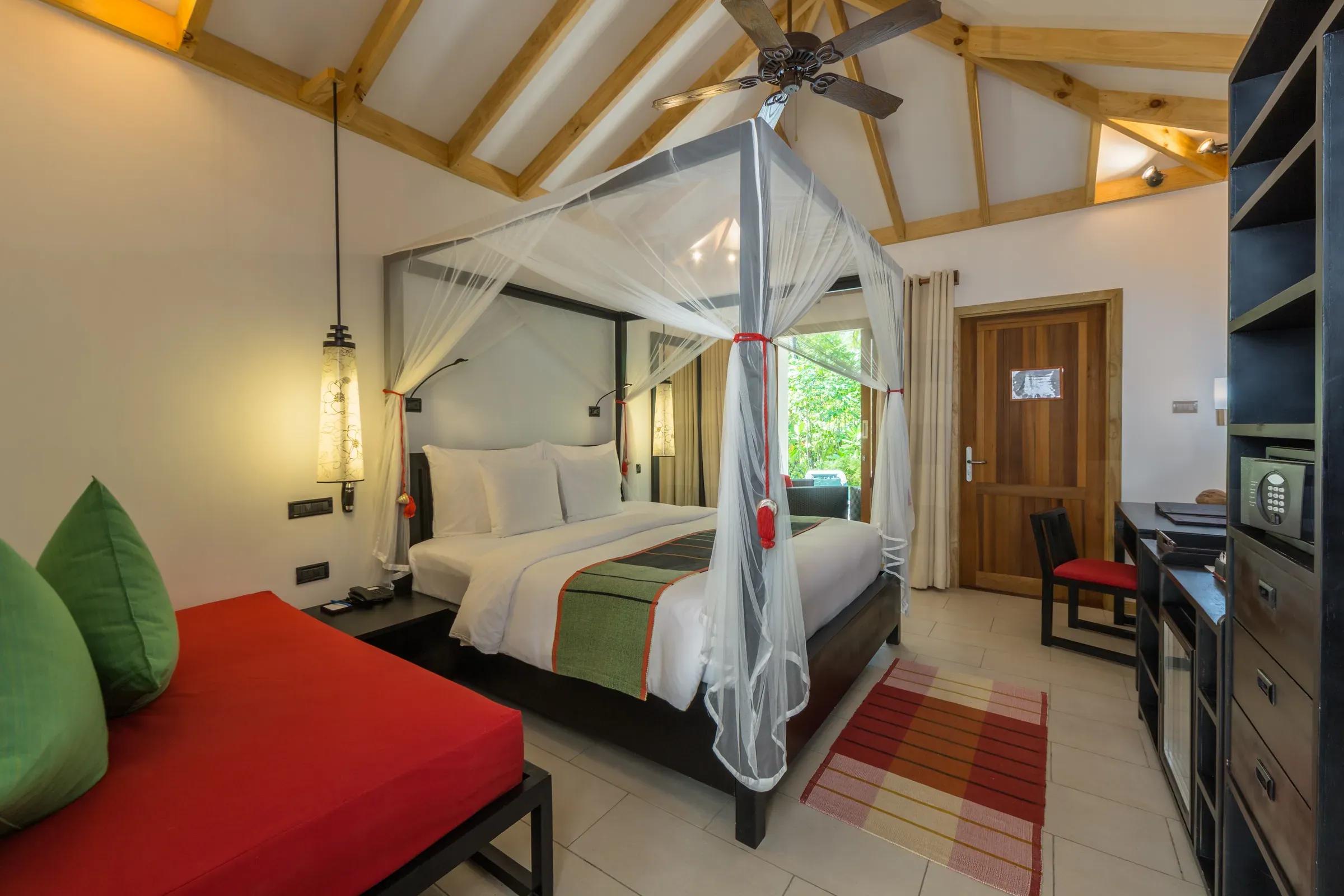 Interno della Tropical Villa con letto a baldacchino e area salotto al Vilamendhoo Maldives.