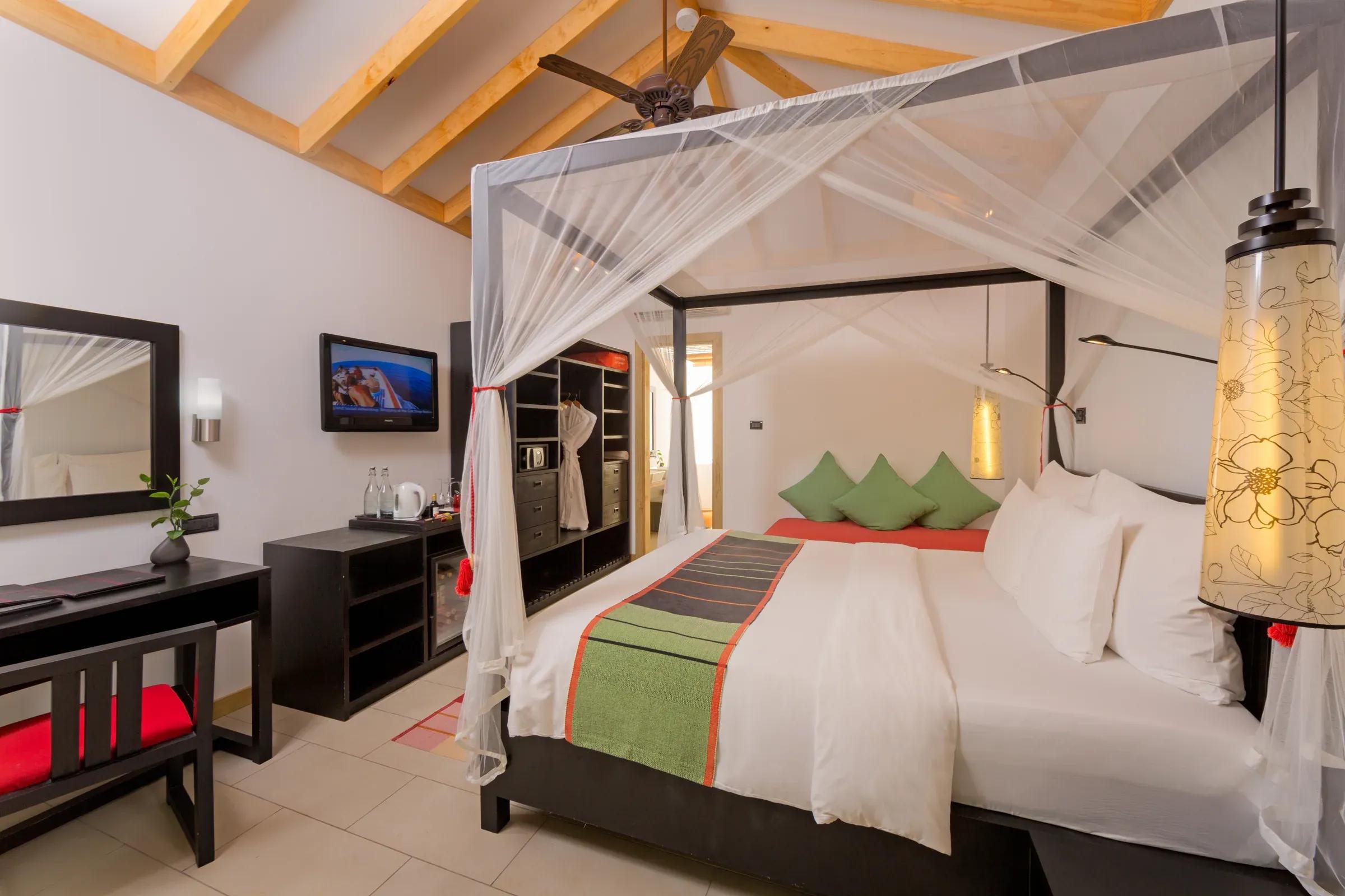 Camera Tropical Villa con letto a baldacchino e scrivania al Vilamendhoo Maldives.
