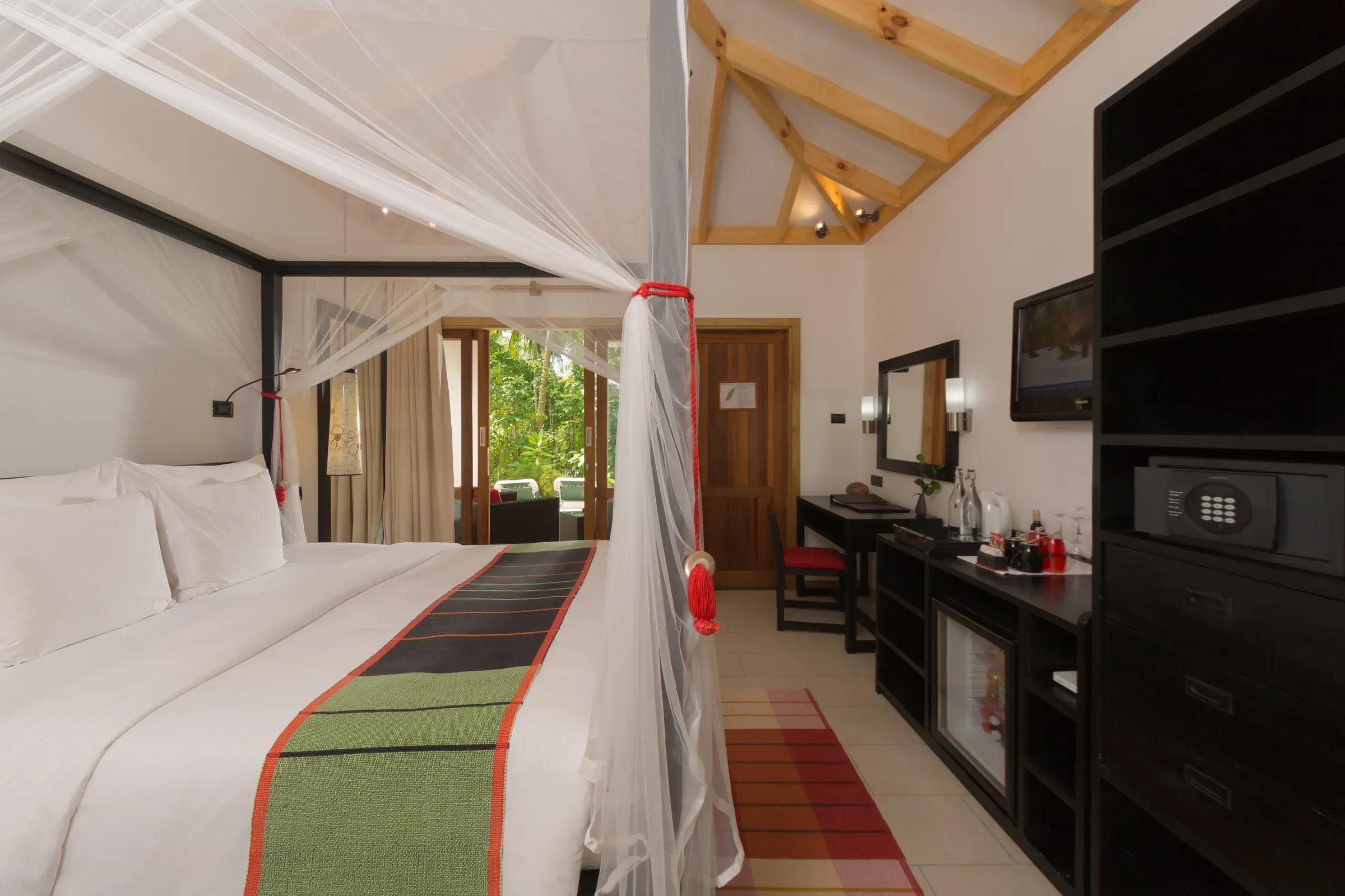 Interno della Garden Room con letto a baldacchino e veranda esterna al Vilamendhoo Maldives.