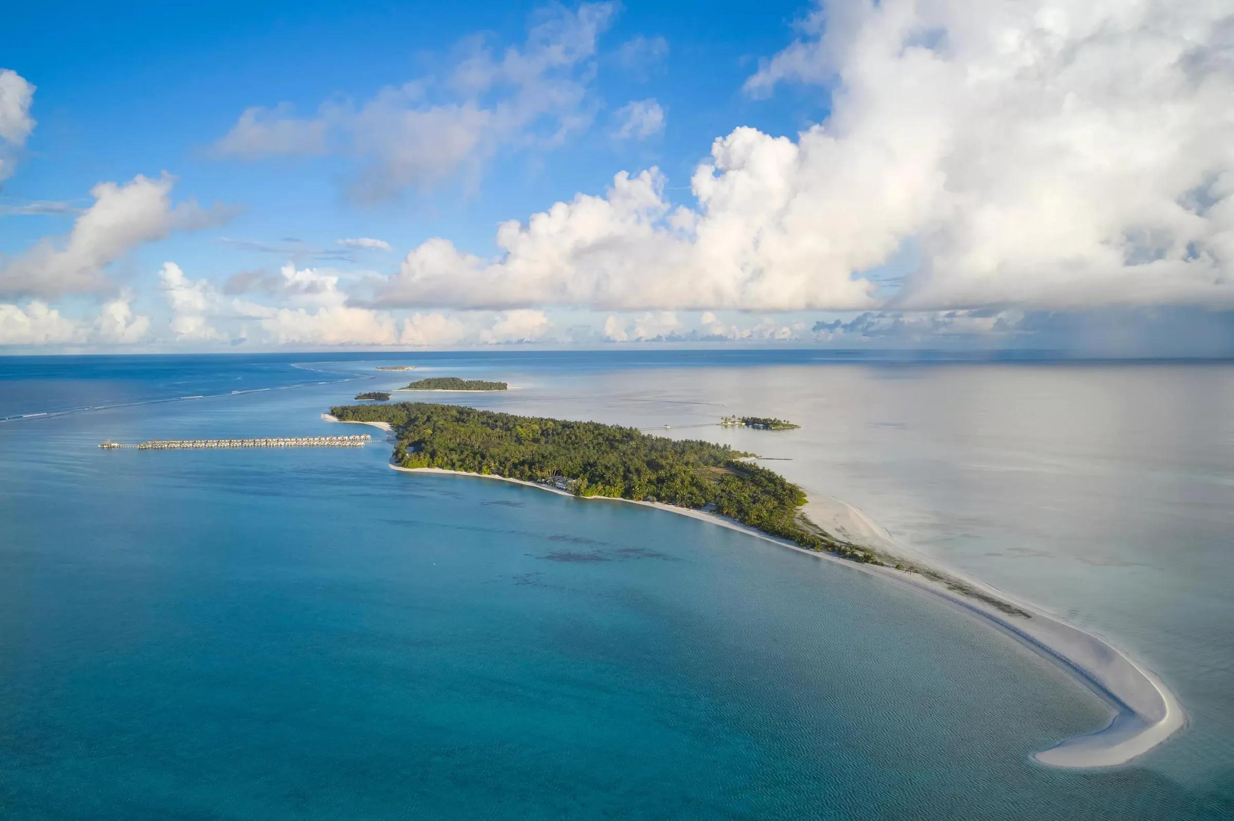 Vista aerea panoramica del Villa Park Sun Island Resort & Spa alle Maldive, un'isola paradisiaca con vegetazione lussureggiante, ville sull'acqua e una magnifica lingua di sabbia bianca nell'oceano turchese.