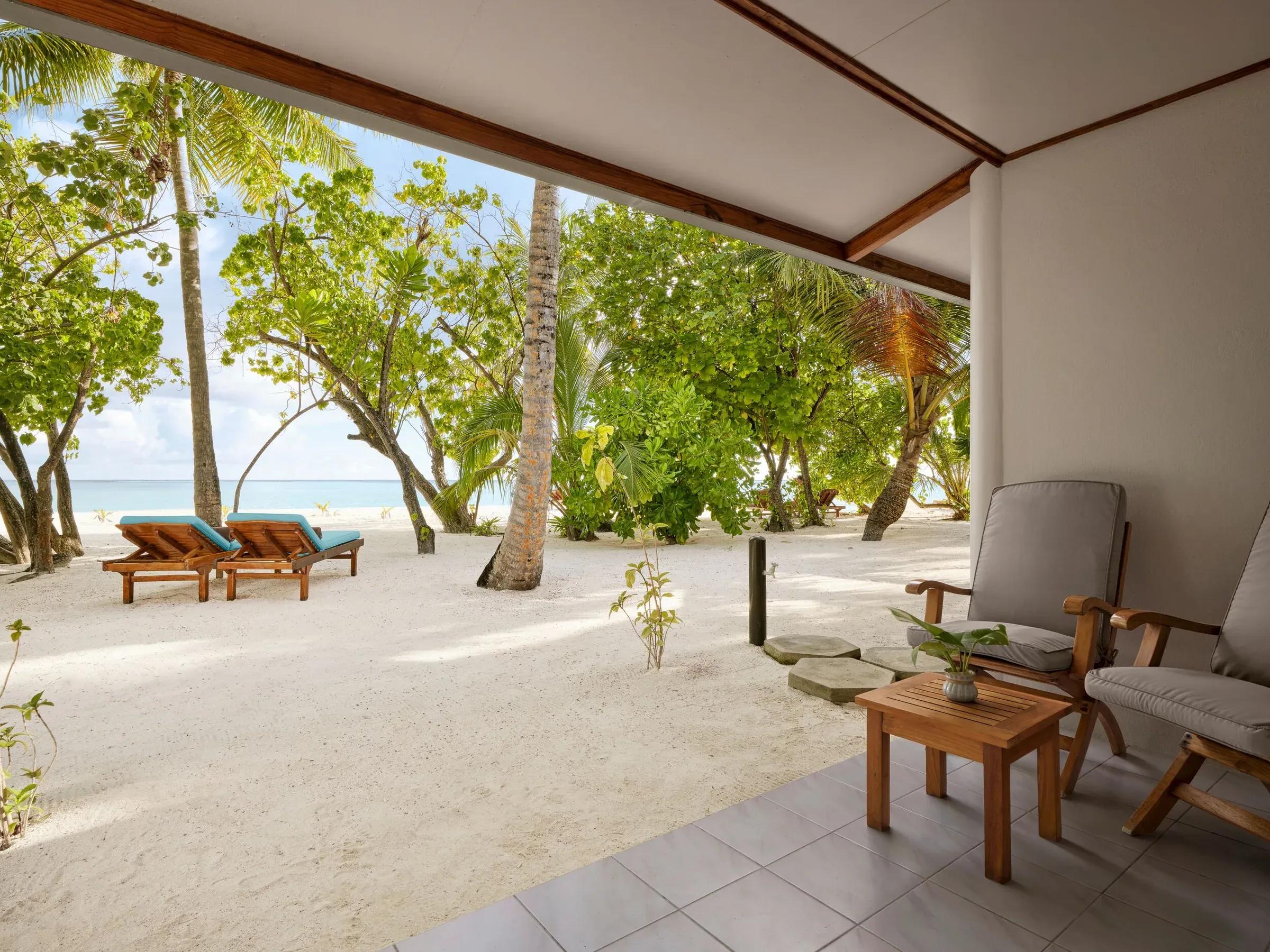 Vista dal patio privato della Beach Villa con accesso diretto alla spiaggia di sabbia bianca e vegetazione lussureggiante al Villa Park Sun Island Resort & Spa. Due comode sedie a sdraio e una piccola area relax invitano a un momento di tranquillità.