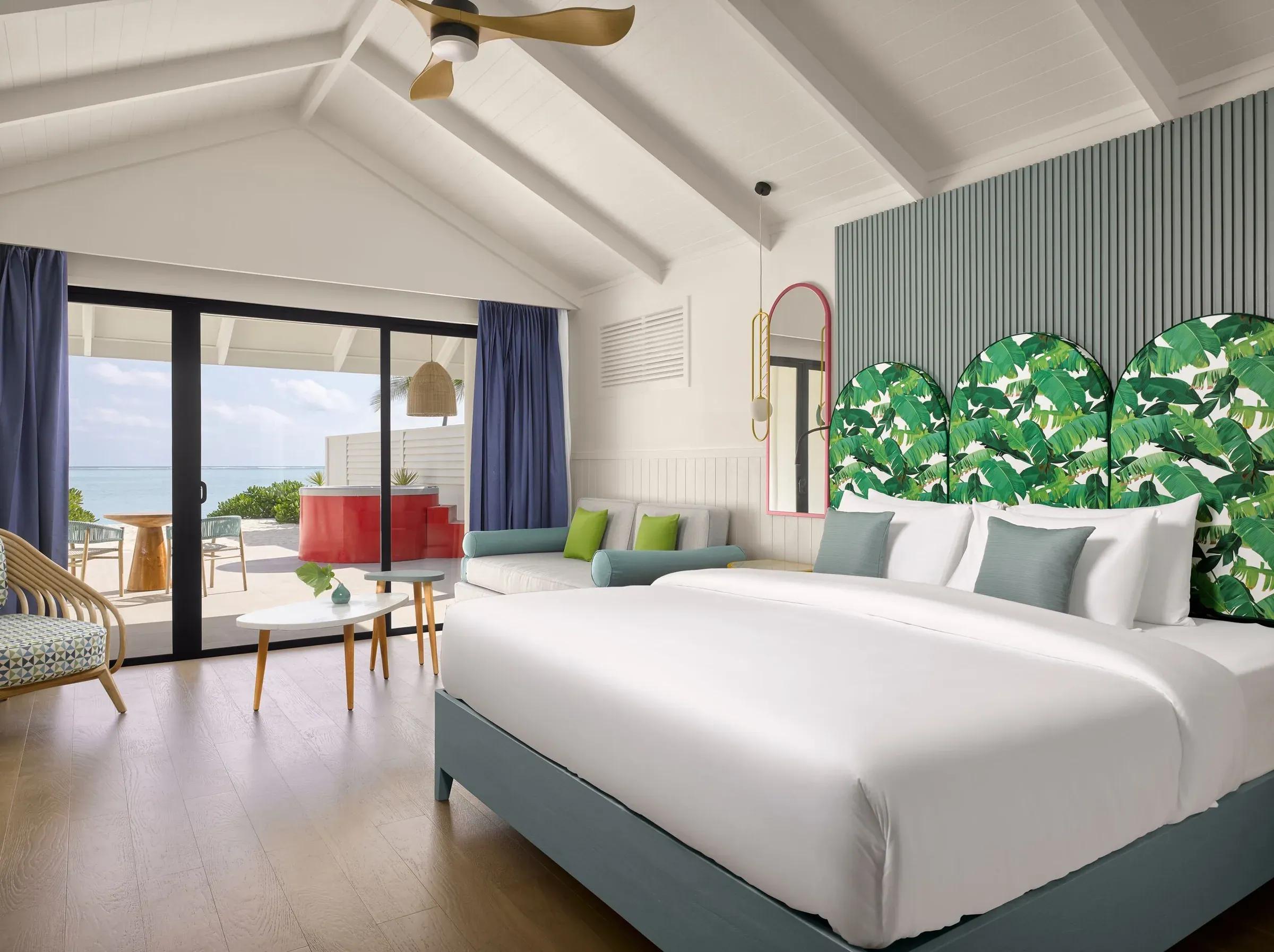 Elegante camera della Beach Villa with Whirlpool al Villa Park Sun Island Resort & Spa, caratterizzata da un letto matrimoniale con testiera tropicale, soffitto a volta e grandi vetrate che offrono una vista panoramica sull'oceano. Accogliente salottino con divano color acqua marina, tavolini moderni e decorazioni di lusso.