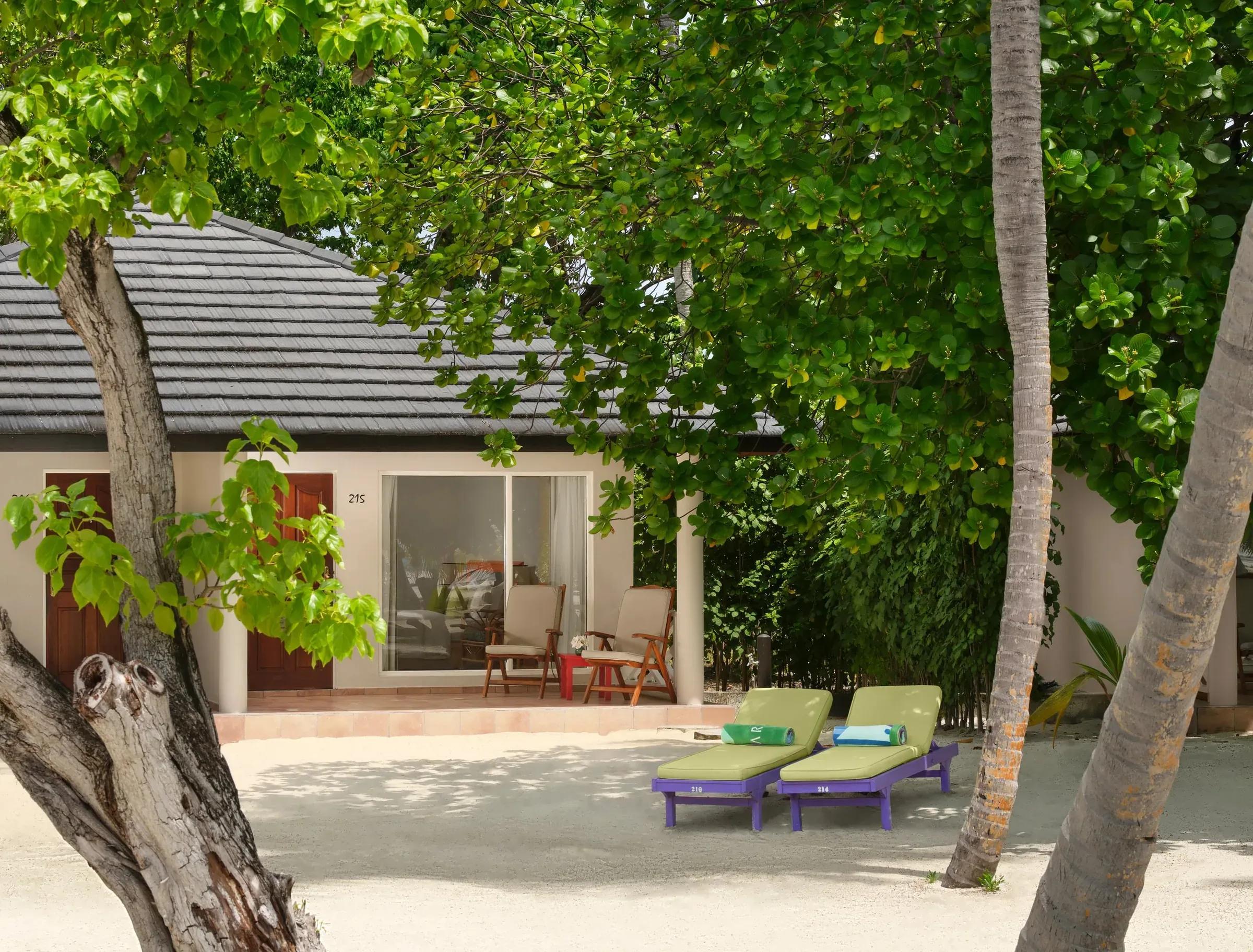 Vista esterna della Island Villa al Villa Park Sun Island Resort & Spa, circondata da lussureggiante vegetazione tropicale. Due lettini invitanti sono posizionati sulla sabbia bianca, ideali per momenti di relax sotto il sole maldiviano.