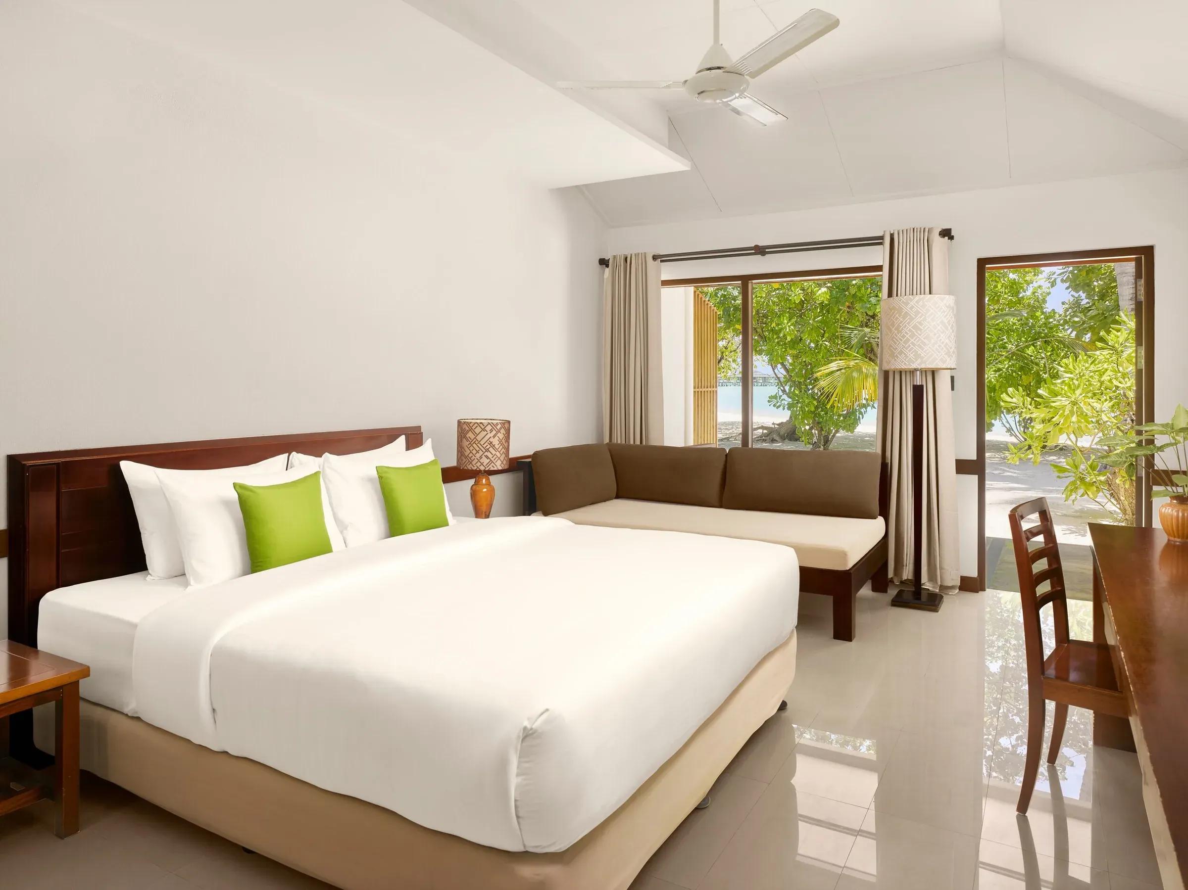 Interno elegante della Sunset Beach Villa con letto king-size e vista mozzafiato sulla spiaggia del Villa Park Sun Island Resort & Spa. Arredamento moderno con dettagli in legno e accenti di verde.