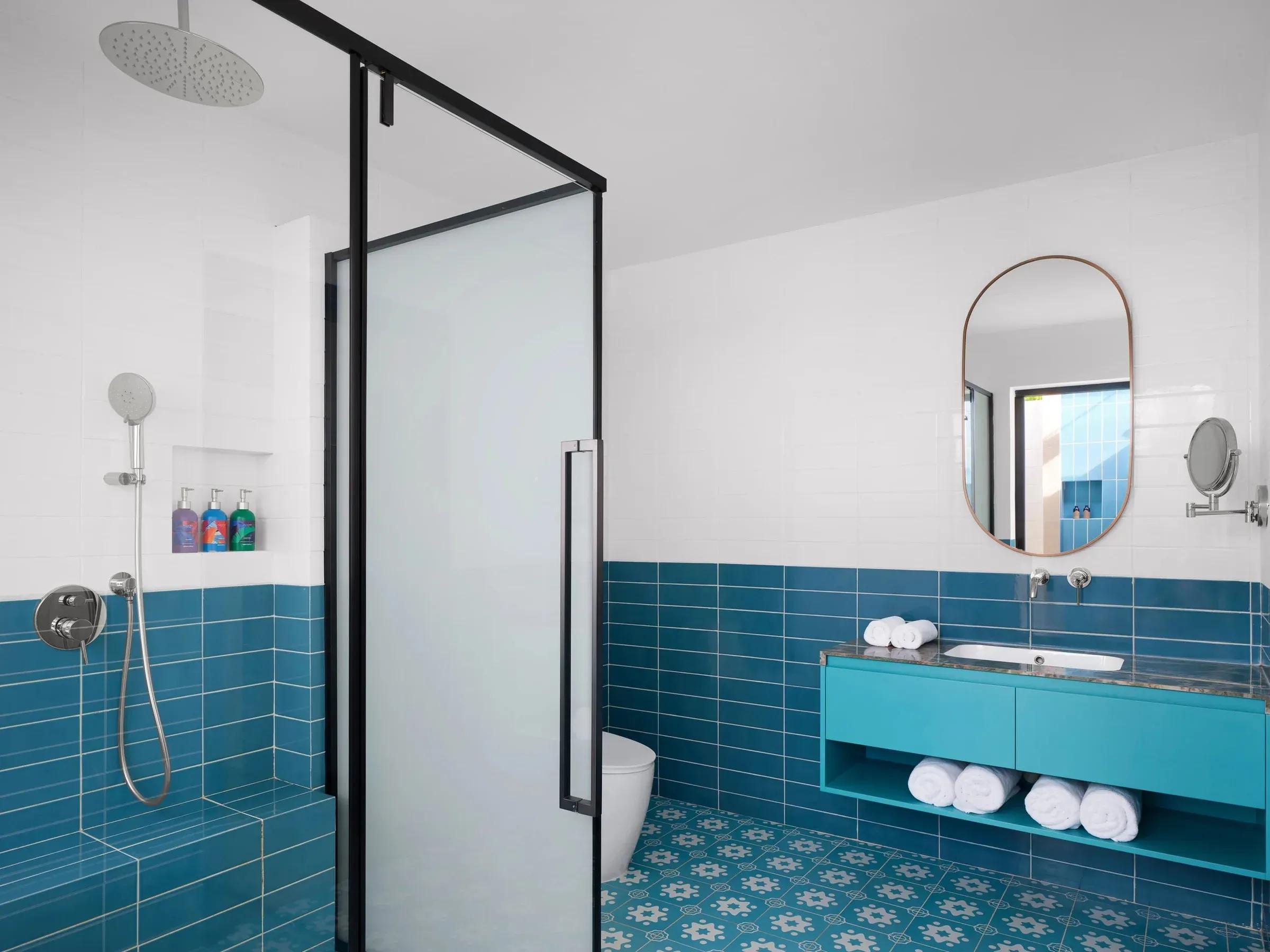 Elegante bagno della Sunset Deluxe Beach Villa al Villa Park Sun Island Resort & Spa, caratterizzato da piastrelle blu, ampia doccia a pioggia e lavabo moderno con specchio ovale.
