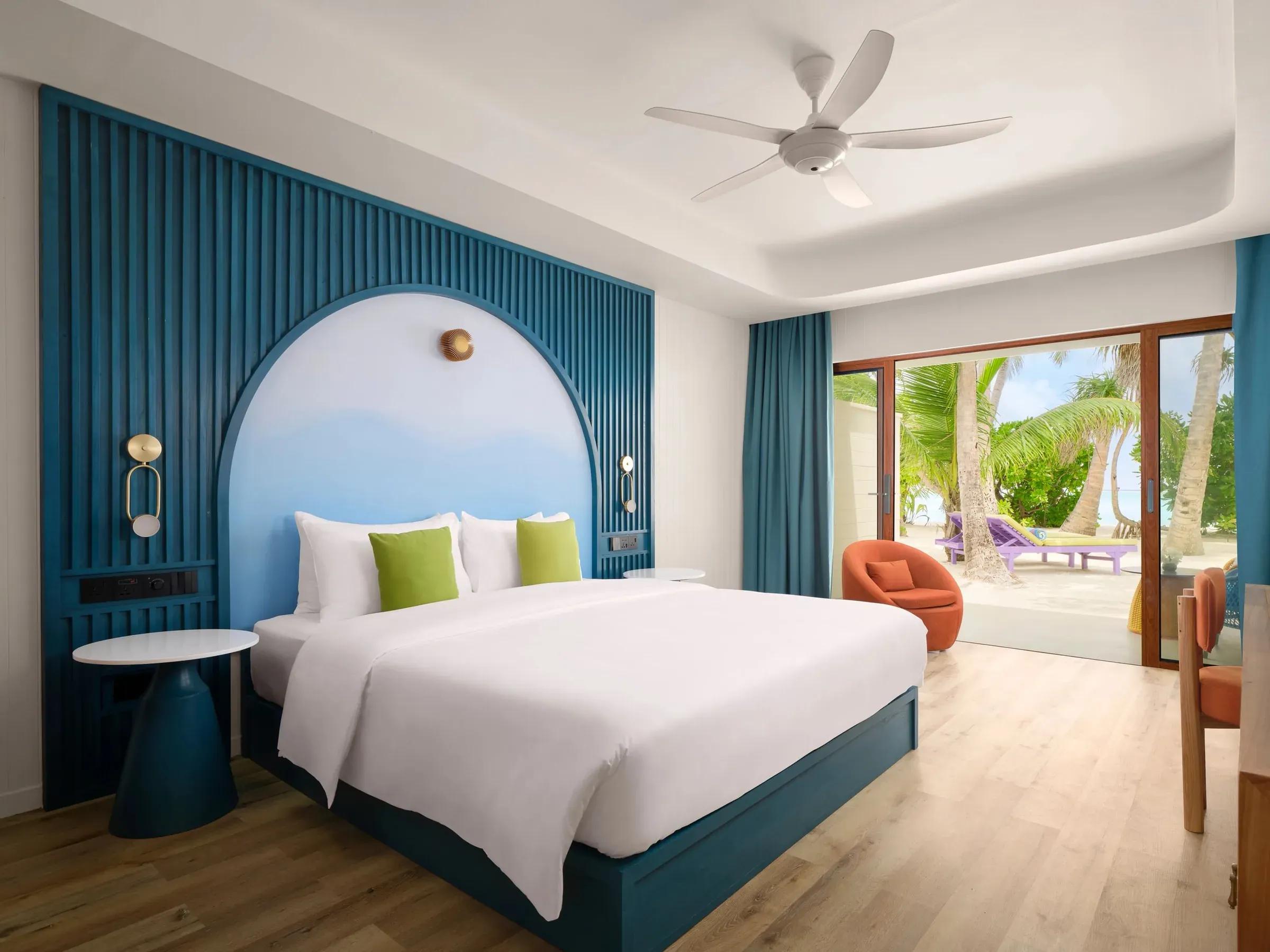 Elegante Sunset Deluxe Beach Villa del Villa Park Sun Island Resort & Spa con letto matrimoniale, interni moderni e vista panoramica sulla spiaggia con palme tropicali dal patio privato.