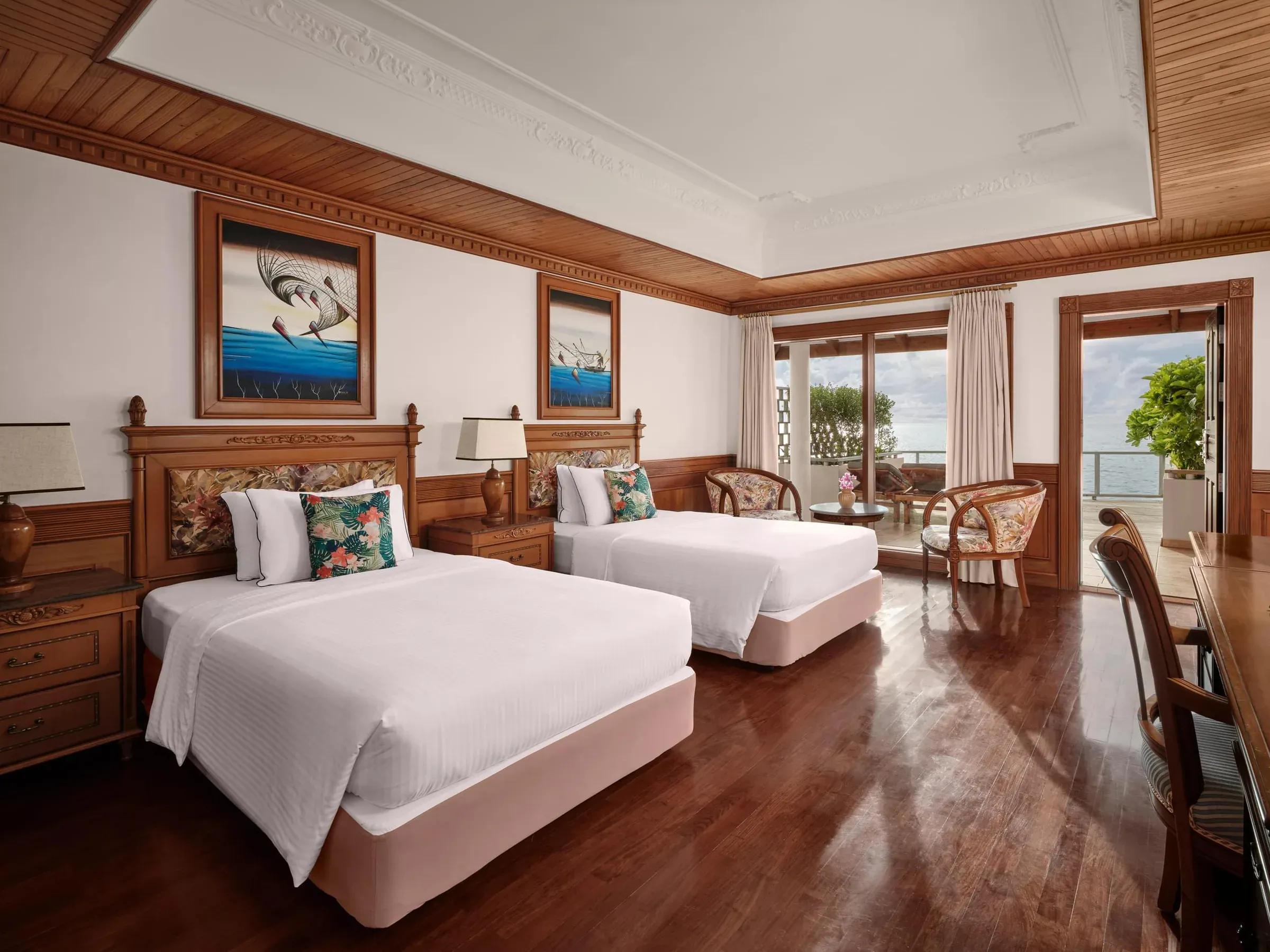Interno della Two Bedroom Overwater Suite con due letti singoli, arredi in legno scuro, pavimento in parquet e accesso alla terrazza privata con vista mozzafiato sull'oceano al Villa Park Sun Island Resort & Spa.