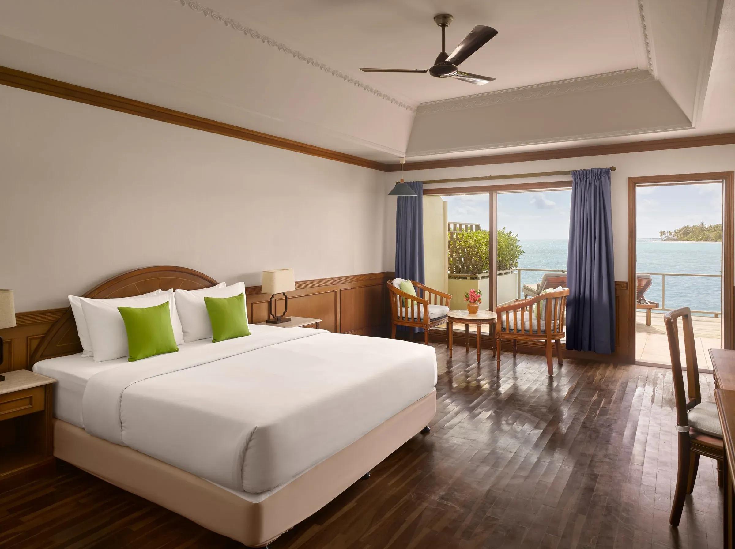 Interno accogliente della Water Villa al Villa Park Sun Island Resort & Spa, con un comodo letto king-size, pavimenti in legno lucido e un'area salotto che si affaccia direttamente sulla terrazza privata e la laguna turchese.